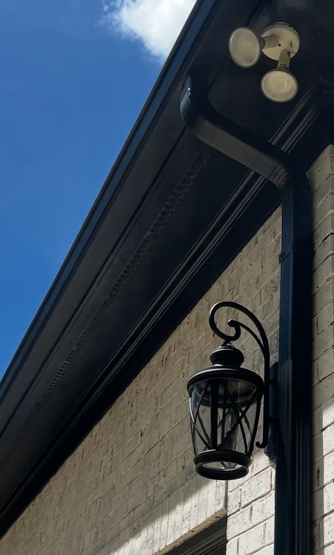 Black gutter and downspout against a light brick wall