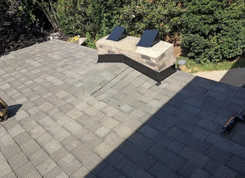 Black metal flashing around a low brick chimney on a shingle roof