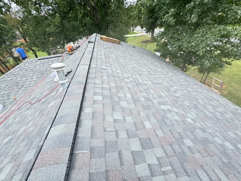 Roofing tools and crew on a gray shingle roof near its ridge