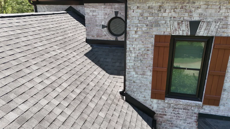 Close view of roof flashing and a black downspout beside white brick dormers